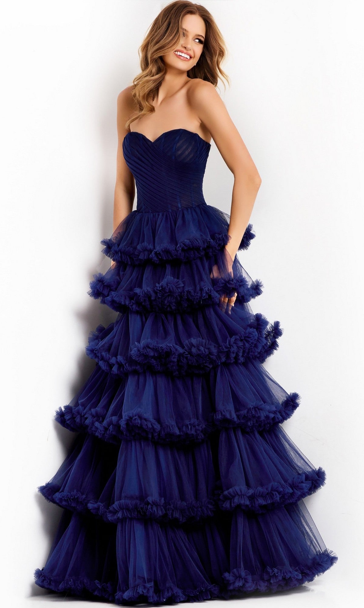 A woman poses against a white background in the elegant Long Prom Dress: Jovani 47139, featuring strapless styling and ruffled tiers with navy blue layers flowing gracefully.